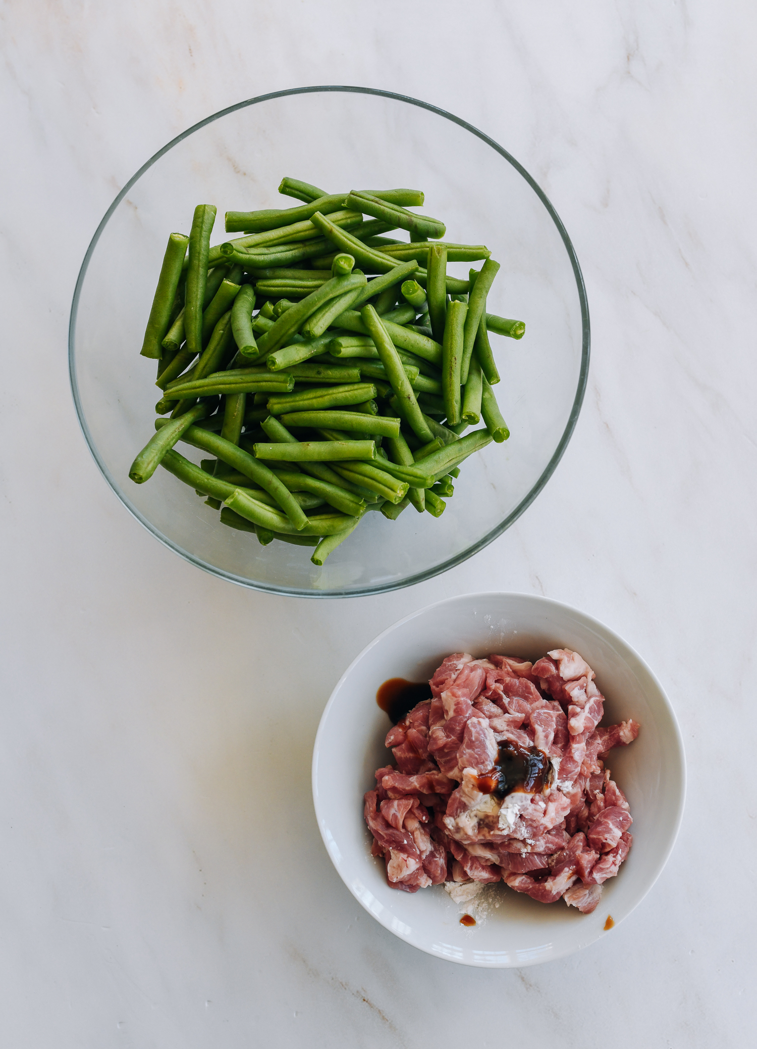 Pork with marinade ingredients and bowl of trimmed green beans