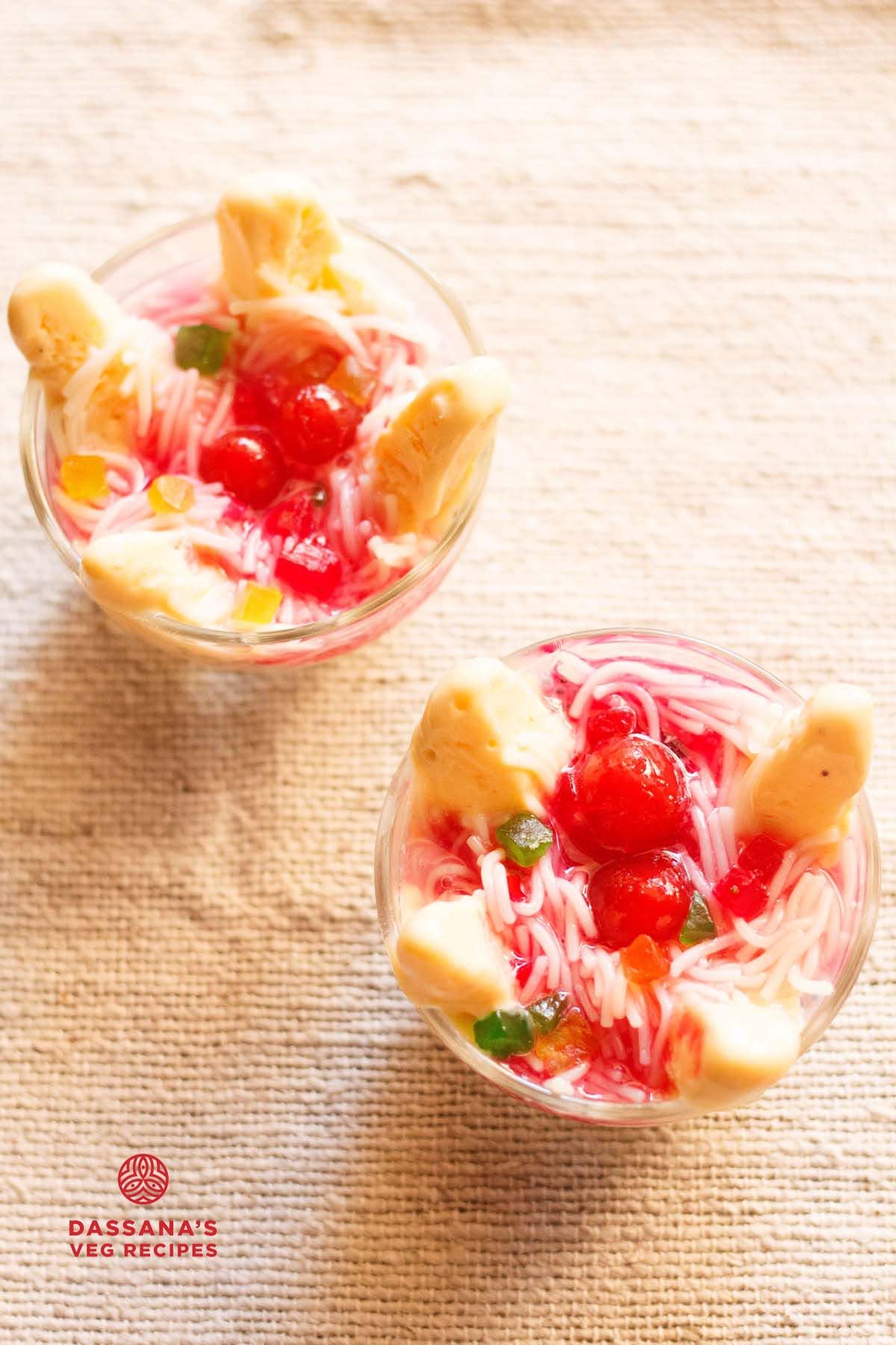 Mango kulfi falooda topped with rose syrup, red cherries, and tutti frutti in bowls.