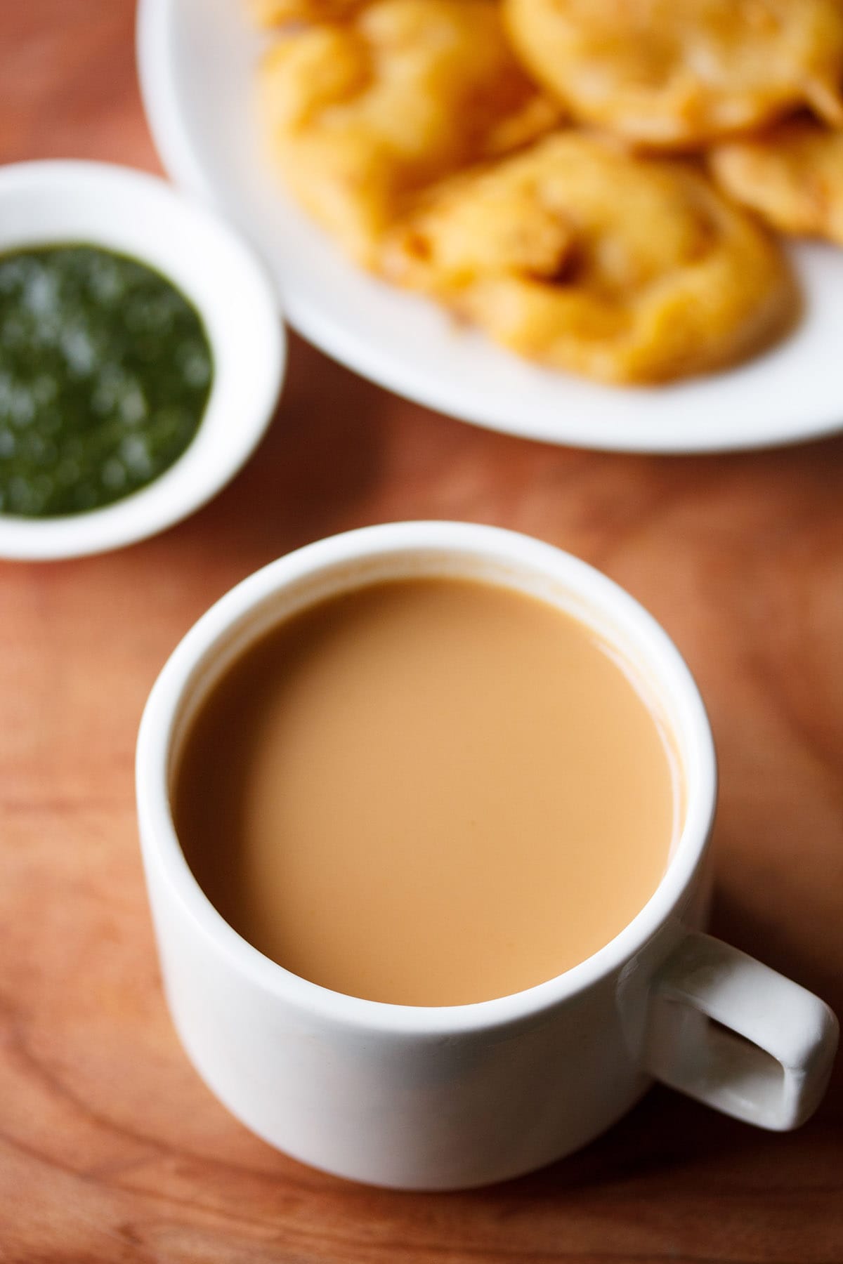 Masala chai filled in a white cup with a side of onion pakora and green chutney