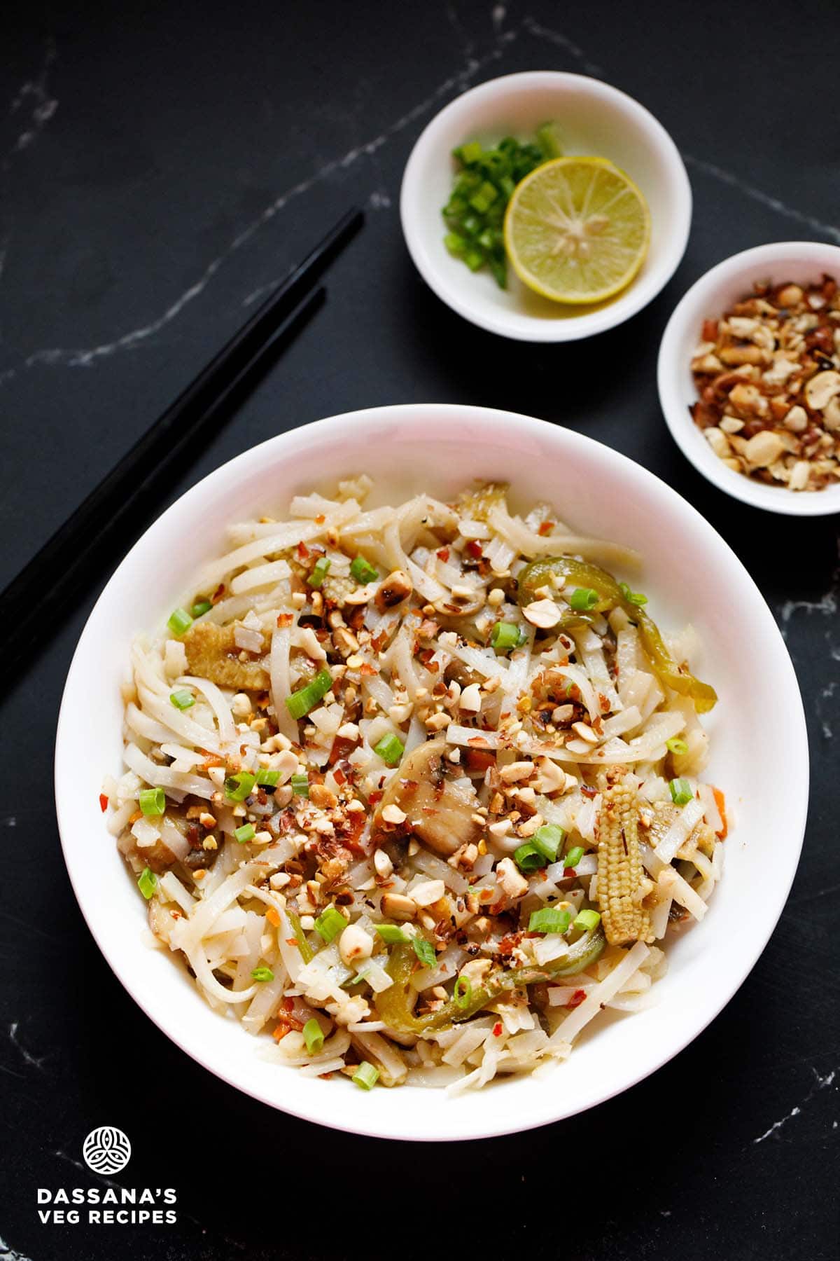 Pad Thai noodles in a white bowl garnished with crushed peanuts and spring onions.