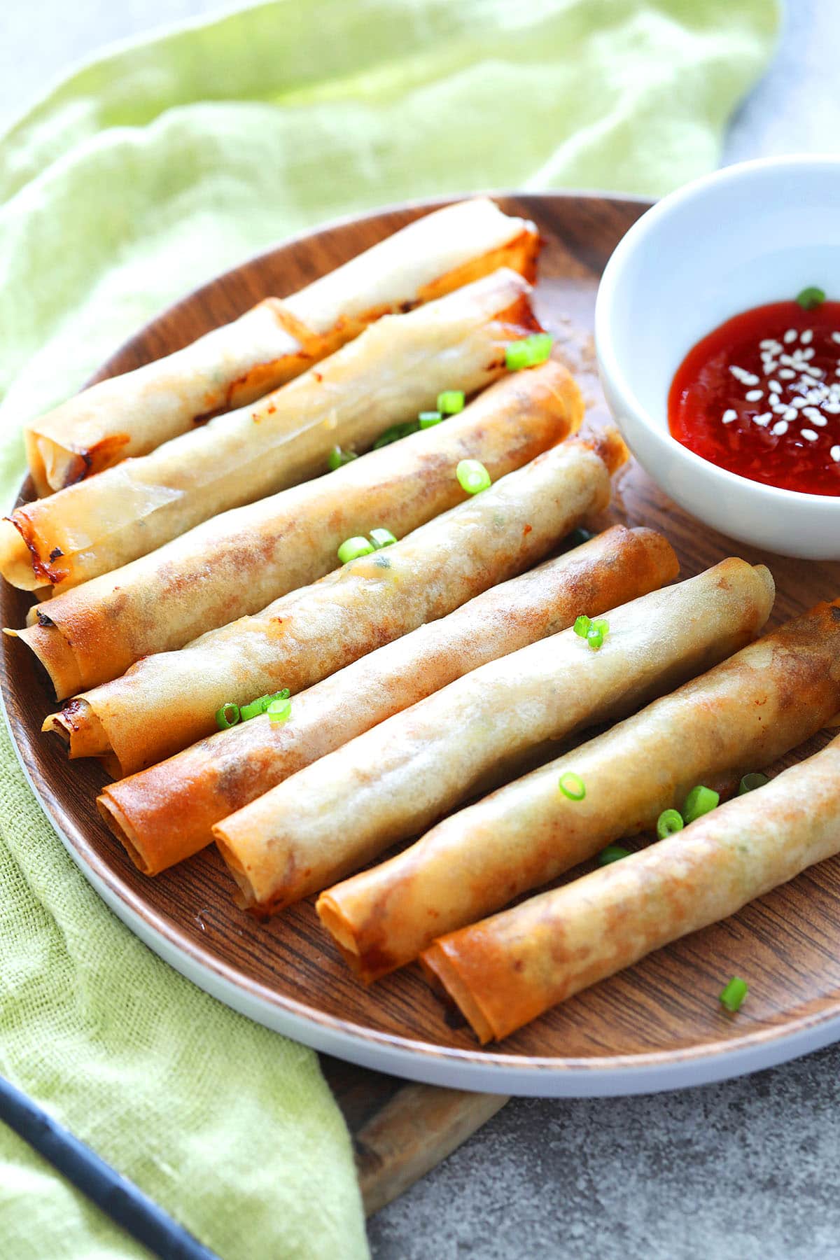 Golden air fryer lumpia on a plate with chili sauce and chopped scallions.