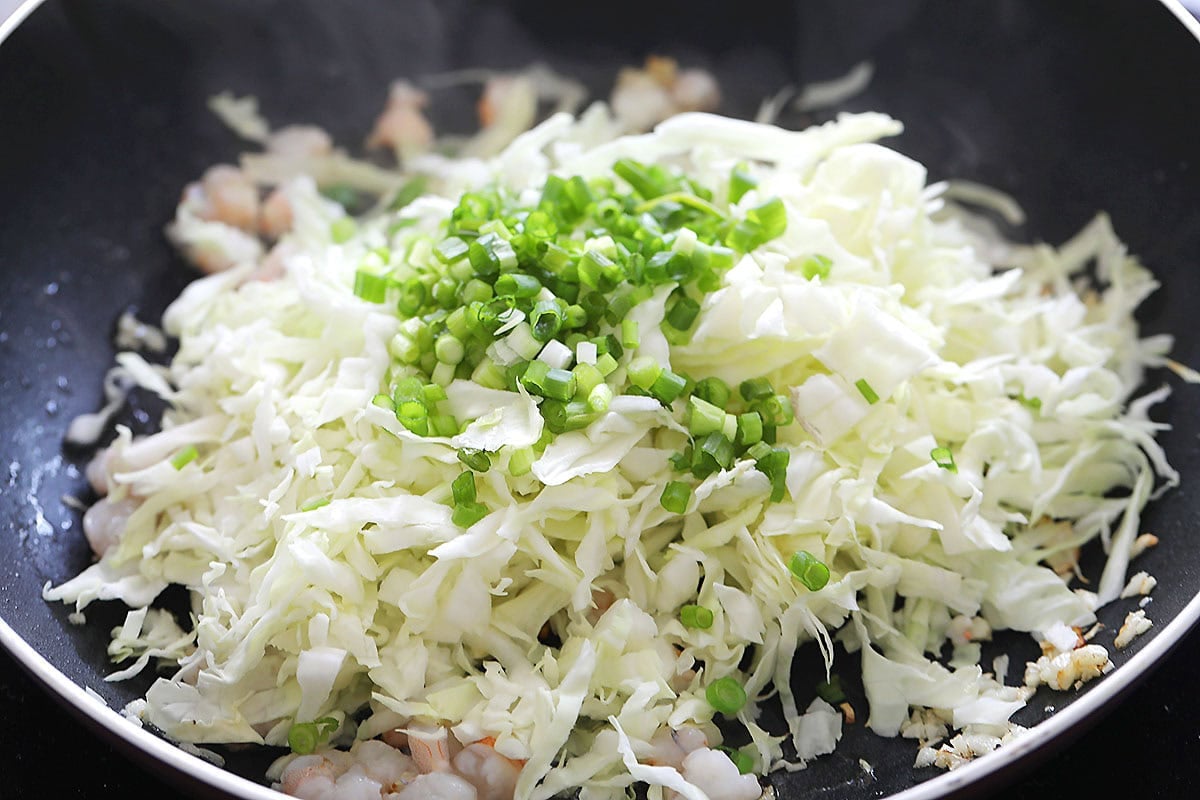 Shrimp, cabbage, and scallion in a skillet.