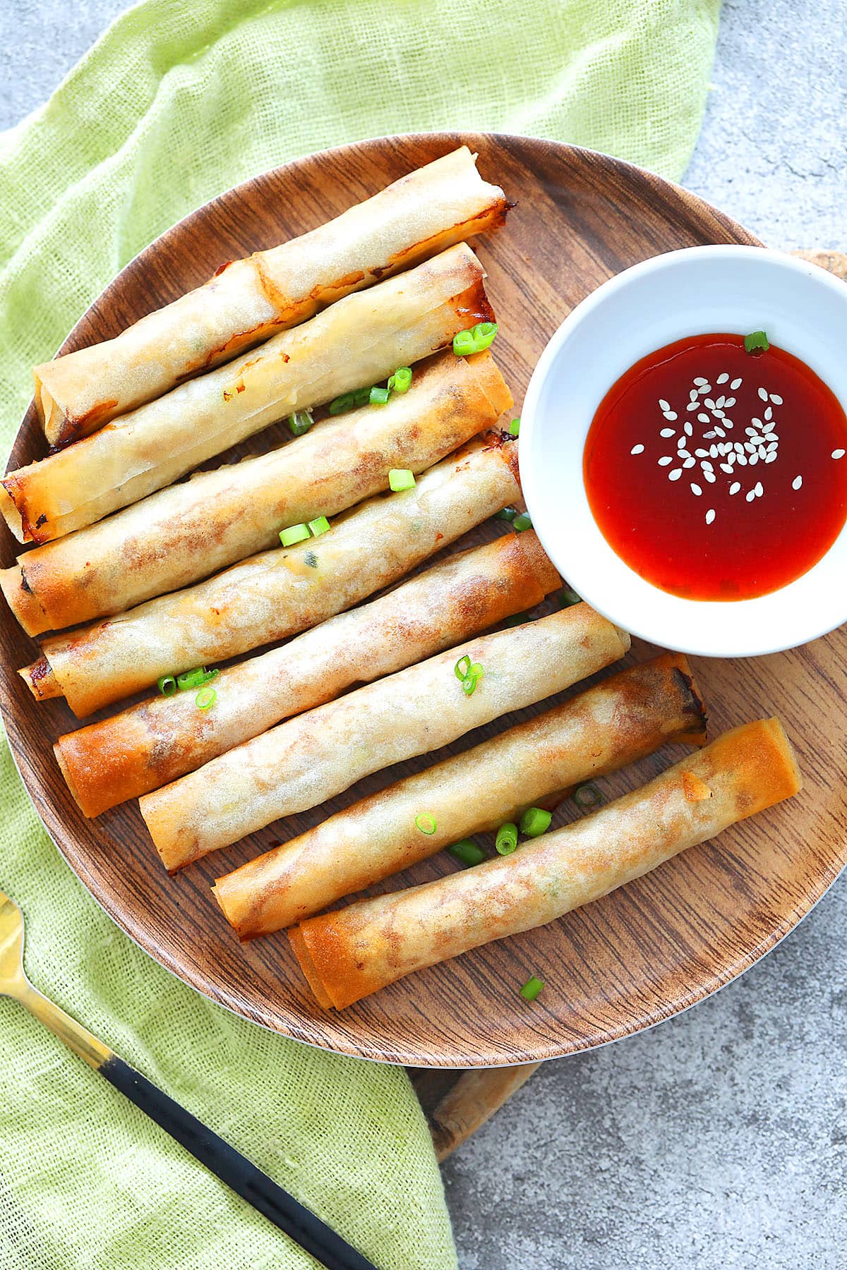 Crispy air fryer lumpia on a white plate next to a bowl of red chili sauce.