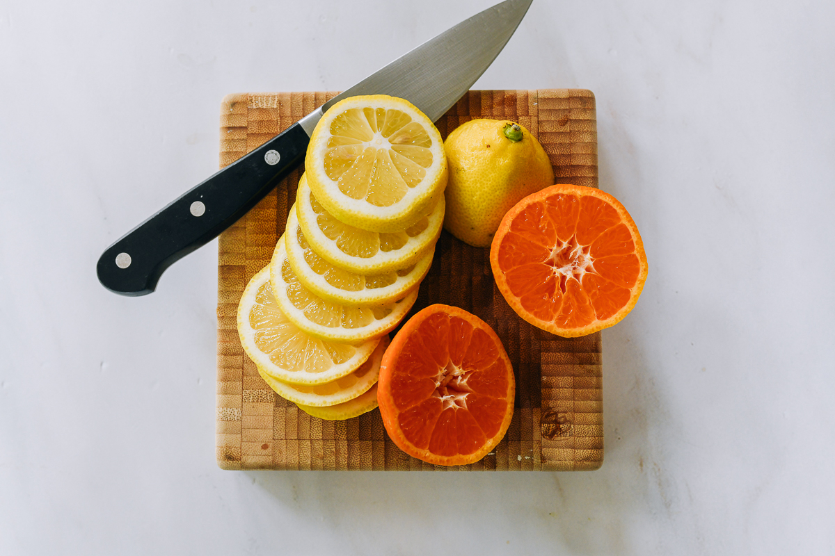 Sliced lemon and halved clementine on cutting board with knife