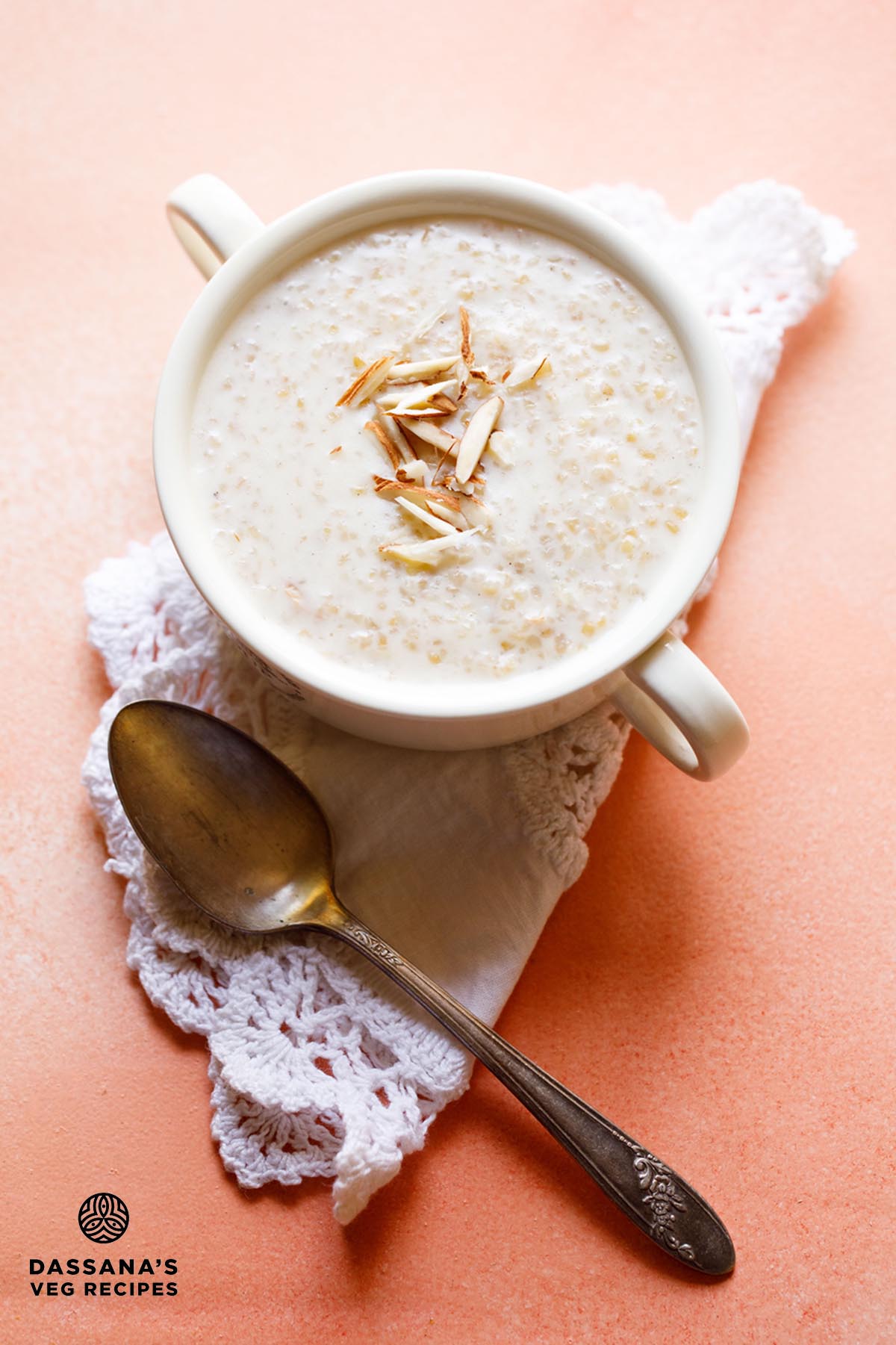 Wheat porridge with slivered almonds in a white bowl with handles on a white folded doily with a brass spoon below.